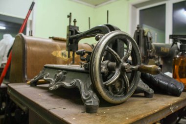 Bir atölyede çekilen eski dikiş makinelerinin yakın plan fotoğrafları, metal parçalar, göstergeler, iğneler ve aşınmış yüzeylere odaklanıyor. Ayrıntılı görüşler, bir crea içinde zanaat, mekanik tasarım ve nostaljik karakter vintage dikiş ekipmanları vurgulanıyor