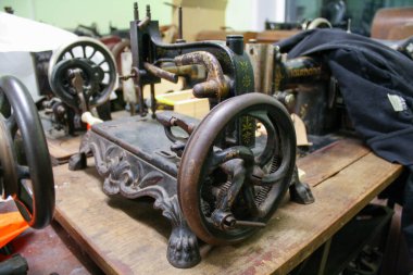 Bir atölyede çekilen eski dikiş makinelerinin yakın plan fotoğrafları, metal parçalar, göstergeler, iğneler ve aşınmış yüzeylere odaklanıyor. Ayrıntılı görüşler, bir crea içinde zanaat, mekanik tasarım ve nostaljik karakter vintage dikiş ekipmanları vurgulanıyor