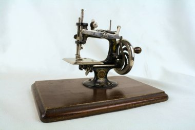 El tekerleği, iğne alanı, metal gövde ve dekoratif elementler gibi farklı mekanik ve tasarım detaylarını gösteren eski bir çocuk dikiş makinesinin fotoğrafları. Yakın çekimler zanaatkarlığı, klasik karakteri ve