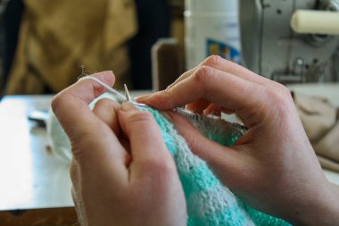 Örgü yaparken bir kadının ellerini gösteren yakın plan bir fotoğraf, örgü iğneleriyle dikkatlice çalışan bir iplik. Görüntü, el işçiliğinin detaylarını yakalıyor, doku, hareket ve örgü örmenin sakin, yaratıcı ritmine odaklanıyor..