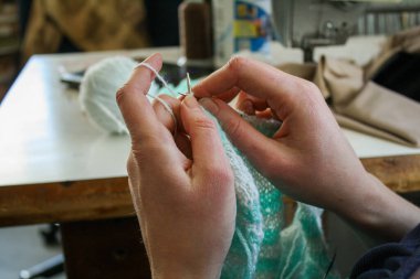 Örgü yaparken bir kadının ellerini gösteren yakın plan bir fotoğraf, örgü iğneleriyle dikkatlice çalışan bir iplik. Görüntü, el işçiliğinin detaylarını yakalıyor, doku, hareket ve örgü örmenin sakin, yaratıcı ritmine odaklanıyor..