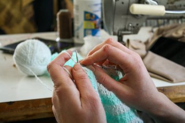 Örgü yaparken bir kadının ellerini gösteren yakın plan bir fotoğraf, örgü iğneleriyle dikkatlice çalışan bir iplik. Görüntü, el işçiliğinin detaylarını yakalıyor, doku, hareket ve örgü örmenin sakin, yaratıcı ritmine odaklanıyor..