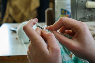 Örgü yaparken bir kadının ellerini gösteren yakın plan bir fotoğraf, örgü iğneleriyle dikkatlice çalışan bir iplik. Görüntü, el işçiliğinin detaylarını yakalıyor, doku, hareket ve örgü örmenin sakin, yaratıcı ritmine odaklanıyor..