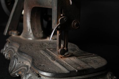 Çok eski, paslı bir dikiş makinesinin ve parçalarının yakından görüntüsü paslanmış metal yüzeyleri, yıpranmış mekanizmaları ve eskimiş detayları gösteriyor. Görüntü, zamanın geçişini ve klasik endüstriyel işçiliğin saf güzelliğini vurguluyor.