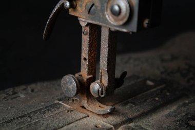 Çok eski, paslı bir dikiş makinesinin ve parçalarının yakından görüntüsü paslanmış metal yüzeyleri, yıpranmış mekanizmaları ve eskimiş detayları gösteriyor. Görüntü, zamanın geçişini ve klasik endüstriyel işçiliğin saf güzelliğini vurguluyor.