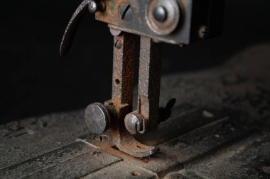 Çok eski, paslı bir dikiş makinesinin ve parçalarının yakından görüntüsü paslanmış metal yüzeyleri, yıpranmış mekanizmaları ve eskimiş detayları gösteriyor. Görüntü, zamanın geçişini ve klasik endüstriyel işçiliğin saf güzelliğini vurguluyor.