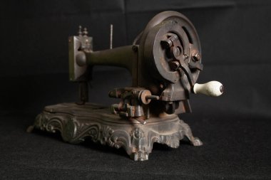 Çok eski, paslı bir dikiş makinesinin ve parçalarının yakından görüntüsü paslanmış metal yüzeyleri, yıpranmış mekanizmaları ve eskimiş detayları gösteriyor. Görüntü, zamanın geçişini ve klasik endüstriyel işçiliğin saf güzelliğini vurguluyor.