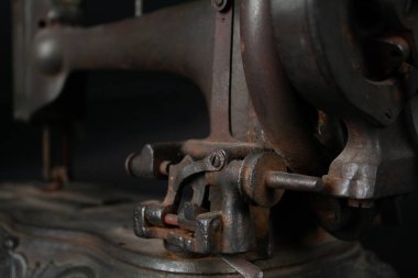 Çok eski, paslı bir dikiş makinesinin ve parçalarının yakından görüntüsü paslanmış metal yüzeyleri, yıpranmış mekanizmaları ve eskimiş detayları gösteriyor. Görüntü, zamanın geçişini ve klasik endüstriyel işçiliğin saf güzelliğini vurguluyor.