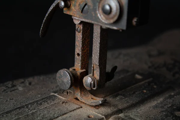Çok eski, paslı bir dikiş makinesinin ve parçalarının yakından görüntüsü paslanmış metal yüzeyleri, yıpranmış mekanizmaları ve eskimiş detayları gösteriyor. Görüntü, zamanın geçişini ve klasik endüstriyel işçiliğin saf güzelliğini vurguluyor.