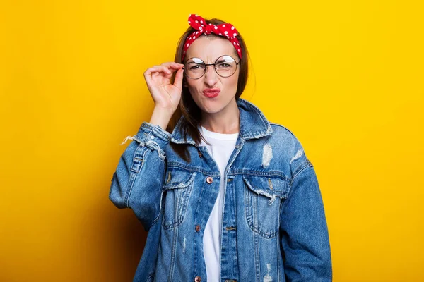 Young woman in a hair band, in a denim jacket with glasses closed her eyes on a yellow background