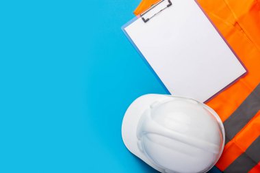İnşaat şapkası, işaret yeleği ve açık mavi arka planda boş bir kağıt. İnşaat ve yenileme işi kavramı. Pankart. Düz yatış, üst görünüm.