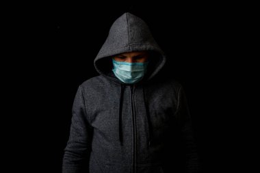 Siyah arka planda eşofmanlı, tıbbi maskeli genç bir adam.