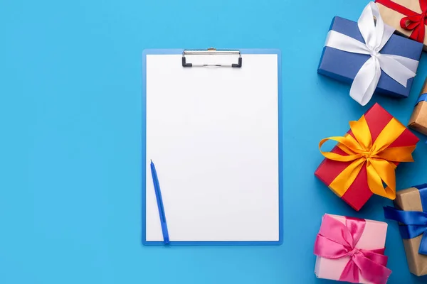 Clipboard with a blank sheet and gifts on a blue background. Gift shopping concept.