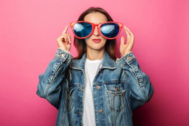 Pembe arka planda kocaman gözlüklü, arkadaş canlısı genç bir kadın.