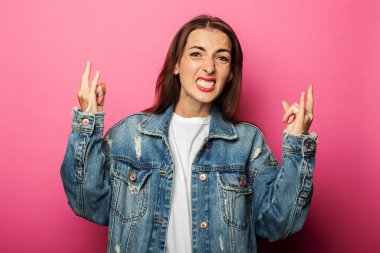 Genç kadın keçi jesti yapıyor, pembe arka planda rockçı kornası.