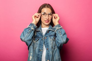 Yuvarlak gözlüklü güzel bir kadın ve pembe arka planda kot ceketli.
