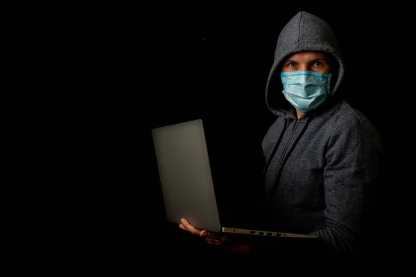 Mann mit Maske und Kapuze hält auf dunklem Hintergrund einen Laptop in der Hand. Konzept von Cyber-Schurke, Hacker. Banner. — Stockbild Mann Mit Maske Und Kapuze Hält Auf Dunklem Hintergrund Einen — Stockfoto