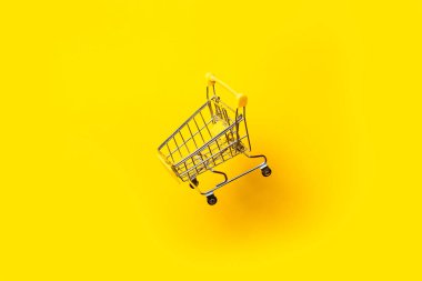 Parlak sarı arka planda havada uçan boş alışveriş arabası..
