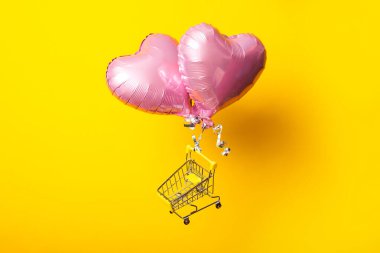 Sarı arka planda pembe kalp şeklinde balonlar üzerinde boş alışveriş arabası sinekleri
