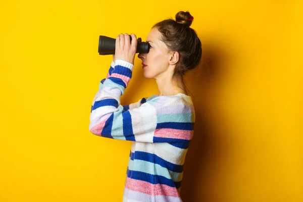 Sarı Arka Planda Dürbünle Bakan Süveterli Genç Bir Kadın — Stok fotoğraf