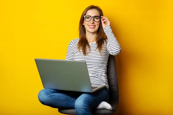 Young woman on chair working at laptop on yellow background.