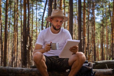 Yürüyüş sırasında elinde harita tutan şapkalı sakallı bir adam. Dağlarda yürüyüş, orman....