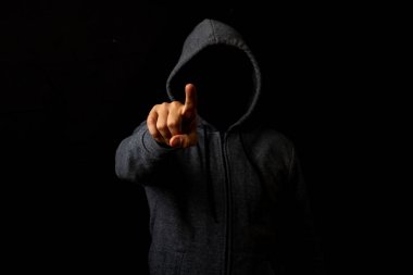 Kapüşonlu yüzü olmayan bir adam karanlık arka planda parmağına dokunur..