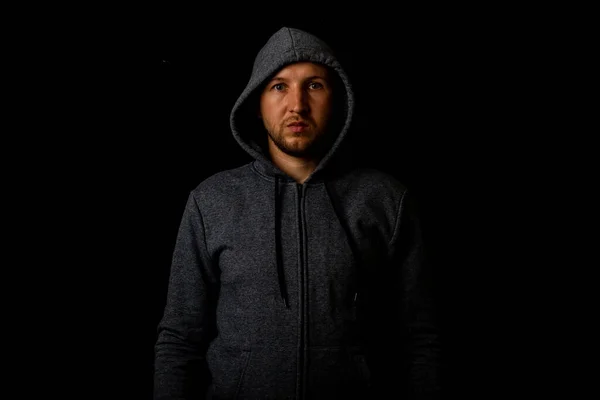 Man in a hood and a hoodie on a dark background.