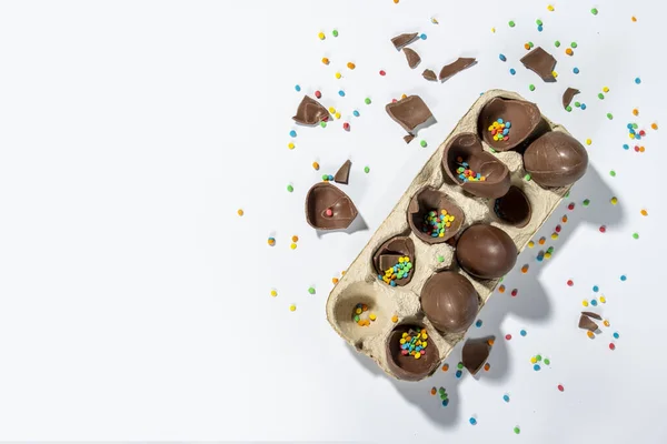 Tray with broken Easter chocolate eggs and multi-colored sweet candy decorations on a light background. Easter concept, easter treats, bunny. Banner. Flat lay, top view.