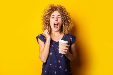 Sarı arka planda, kıvırcık saçlı, uykulu, esneyen genç bir kadın.