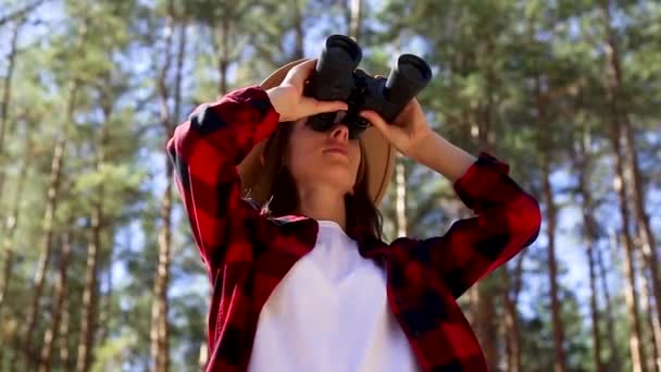 Şapkalı kız ormandaki dürbünle bakıyor. Yürüyüş kavramı, turizm. — Stok video