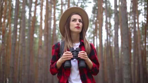 Mujer turista con prismáticos mira alrededor en el bosque. Concepto caminata, turismo. — Vídeo de stock