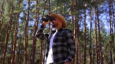 Erkek turist ormandaki dürbünle bakar. Kompozisyon yürüyüşü, ormancı.