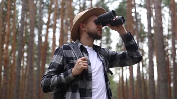 Hombre turista con una mochila mira a través de los prismáticos, mientras que el senderismo en el bosque o las montañas. Concepto de senderismo. — Vídeo de stock