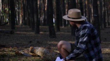 Genç adam gün batımında dağlarda veya ormanda yürürken bir kütüğün üzerinde dinleniyor..
