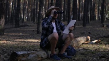Genç adam dinleniyor, dürbünle bakıyor ve yürürken haritaya bakıyor.