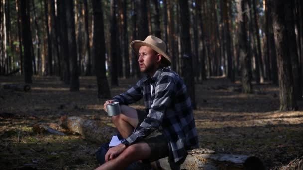 Joven descansando en un tronco mientras camina por las montañas o el bosque al atardecer. — Vídeo de stock