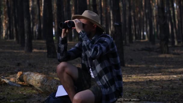 Mladý muž odpočívá na kládě a dívá se dalekohledem při pěší túře — Stock video