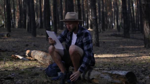 Mladý muž odpočívá a kontroluje mapu při pěší túře v horách nebo lesích — Stock video