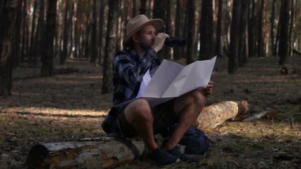 Young man resting, looking through binoculars and checking a map while hiking — Stock Footage Young man resting, looking through binoculars and checking a map while hiking Video Clip