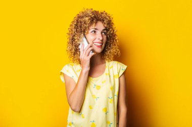 Sarı arka planda telefonla konuşan, gülümseyen kıvırcık bir genç kadın.