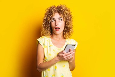 Güzel kıvırcık bir kadın sarı arka planda telefon tutarken şaşırdı.