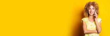 Sarı arka planda telefonda gülümseyen kıvırcık, genç bir kadın. Pankart
