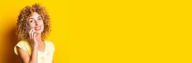 Sarı arka planda telefonda gülümseyen kıvırcık, genç bir kadın. Pankart