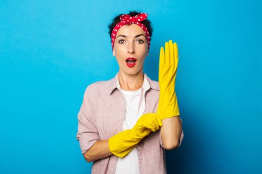 Mavi arka planda temizlik eldivenleri olan tişörtlü genç bir kadın.