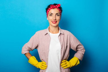 Saçları kırmızı bandajlı, eldivenleri mavi arka planı temizleyen güzel bir kadın.