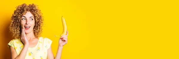 Curly Young Woman Looks Surprised Holding Yellow Banana Yellow Background — Stock Photo, Image