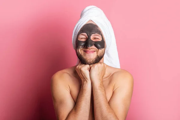 smiling young man with cosmetic mask on pink background. Skin care concept.