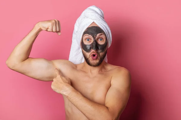 surprised nude man with cosmetic mask on his face, points finger showing muscle on pink background.
