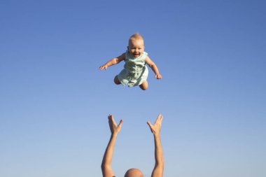 Adam bebeği mavi gökyüzüne fırlatıyor. Çocuklarla konsept oyun, mutlu aile.